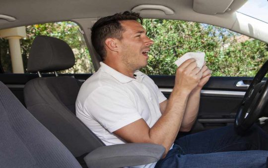 Uomo che starnutisce in auto per allergia